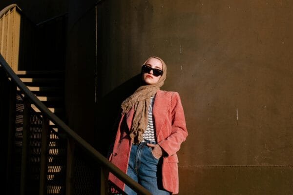 Fashionable woman wearing hijab and sunglasses posing by urban staircase, exuding confidence.