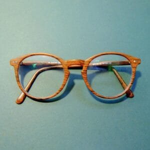 Close-up of fashionable wooden frame eyeglasses on a solid blue background.
