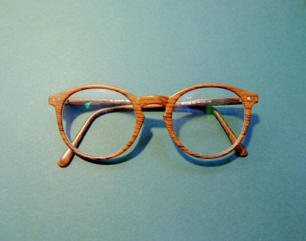 Close-up of fashionable wooden frame eyeglasses on a solid blue background.